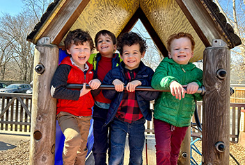 4 students smiling on top of a wooden playground structure